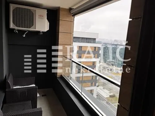 Small enclosed balcony with seating furniture and city view.