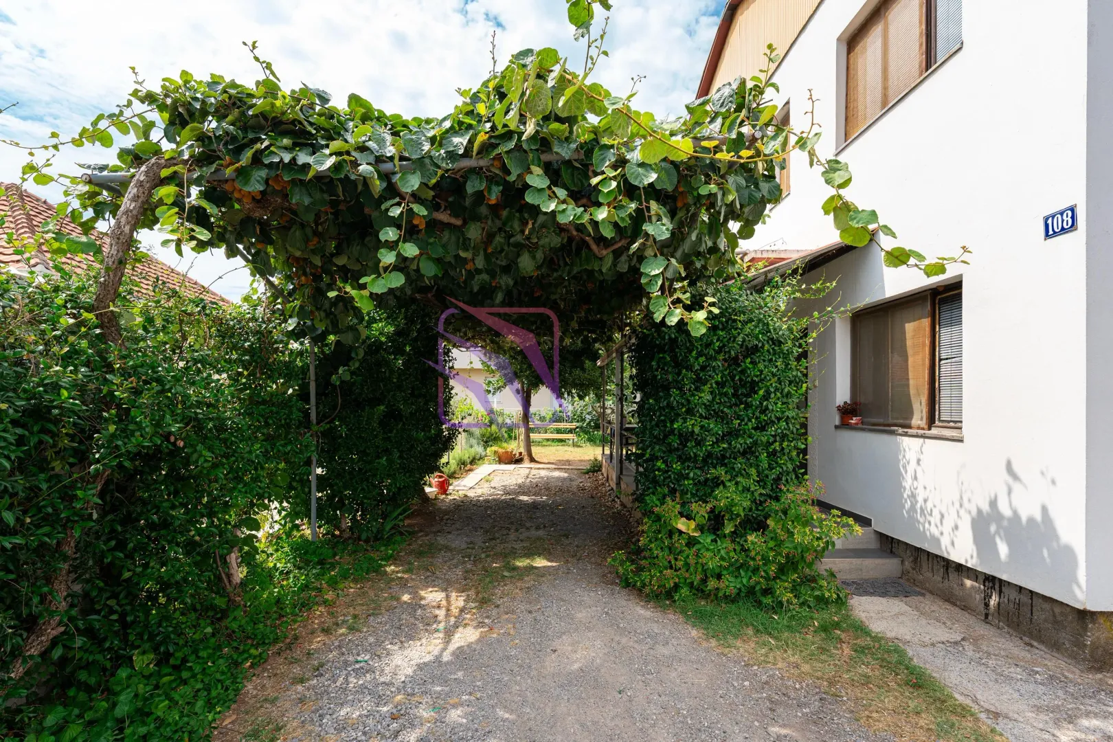 Pogled na dvorište i natkriveni prilaz sa zelenilom pored kuće.