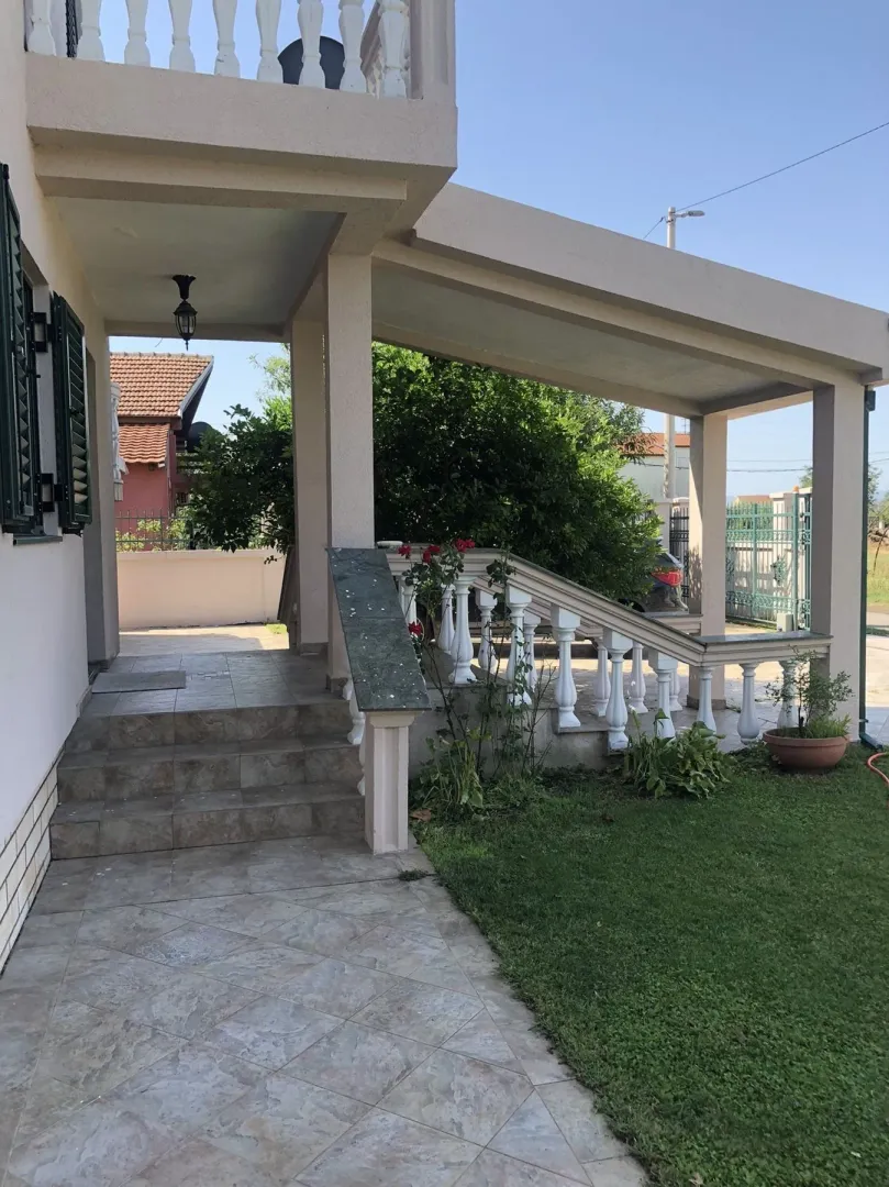 A tiled pathway and covered entrance to a house with a landscaped yard.