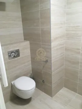 Pogled na kupatilo sa zidnim toaletom obloženo bež pločicama. - image 15