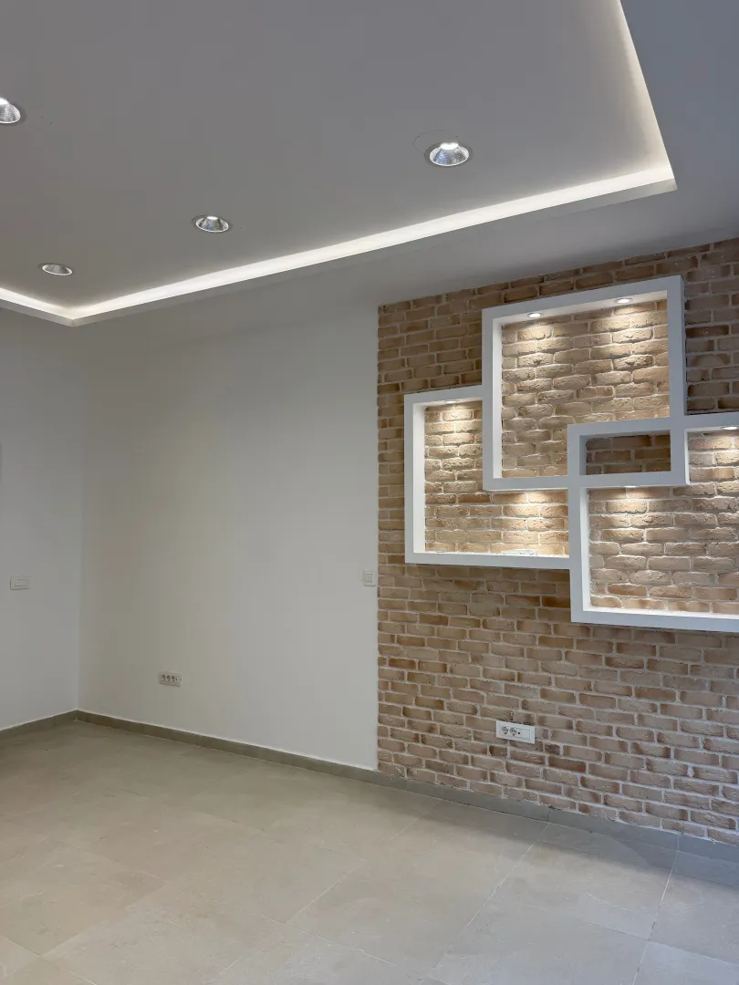 Empty living room with a decorative brick wall and recessed lighting.