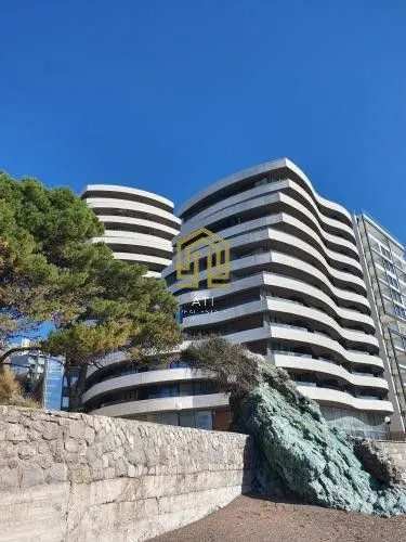 Spoljašnji izgled moderne višestambene zgrade sa terasama i kamenim zidom u prvom planu.