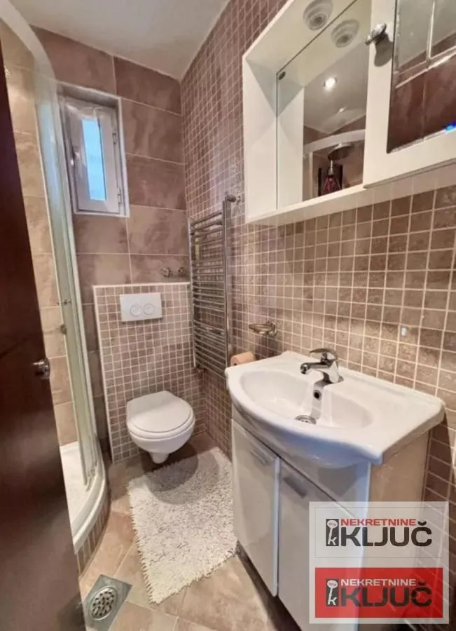 Kupatilo obloženo keramičkim pločicama sa umivaonikom, WC šoljom i tuš kabinom.