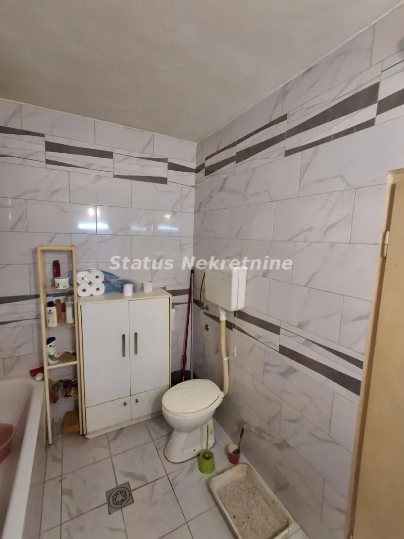 Manje kupatilo obloženo keramičkim pločicama sa toaletom, ormarićem i kadom.