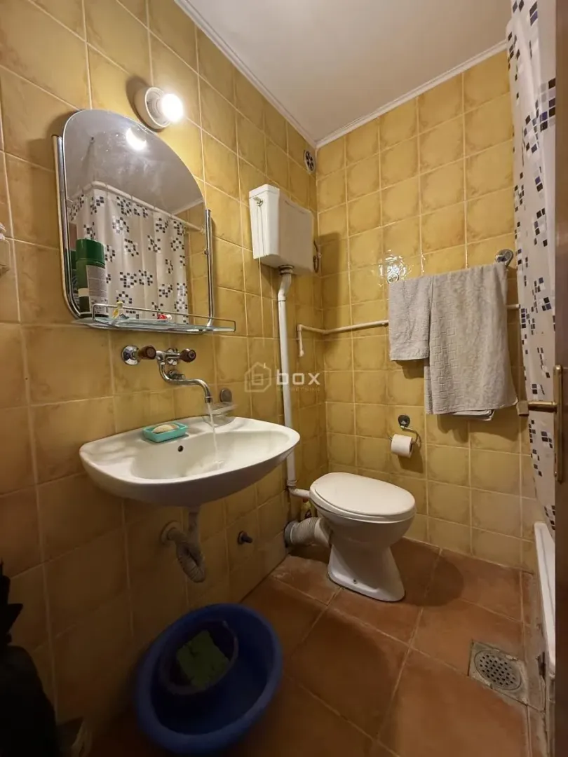 Manje kupatilo obloženo žutim pločicama sa umivaonikom i wc šoljom.