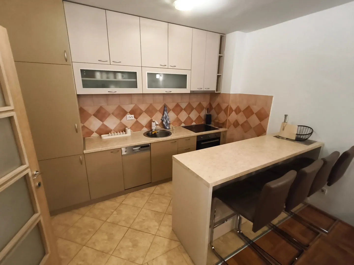 Kuhinja opremljena elementima i šankom sa barskim stolicama.