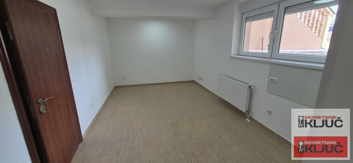 Prazna neopremljena soba sa laminatom, drvenim vratima i prozorom.