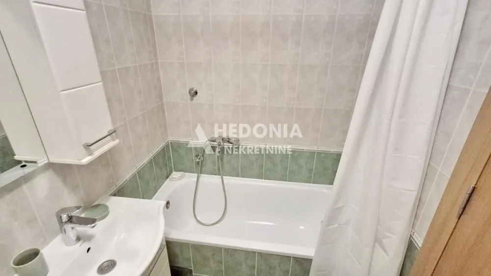 Small bathroom with a bathtub, washbasin, and wall tiles.