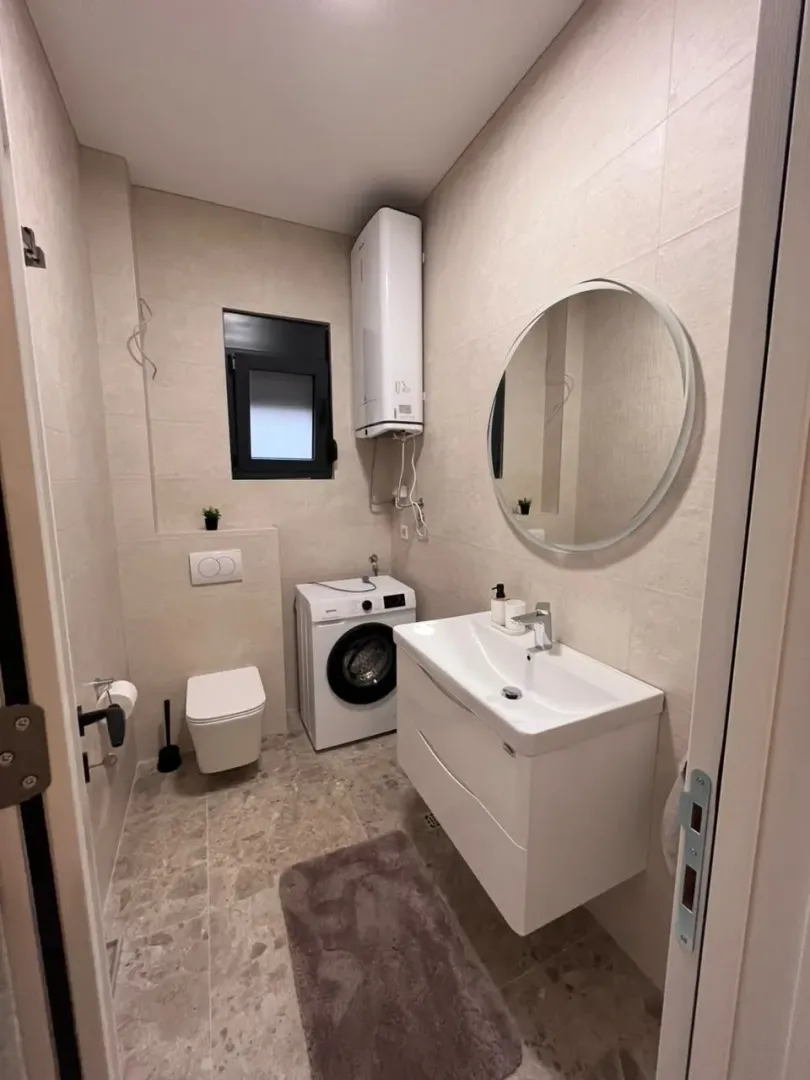 Smaller bathroom with a sink, toilet, washing machine, and a round mirror.