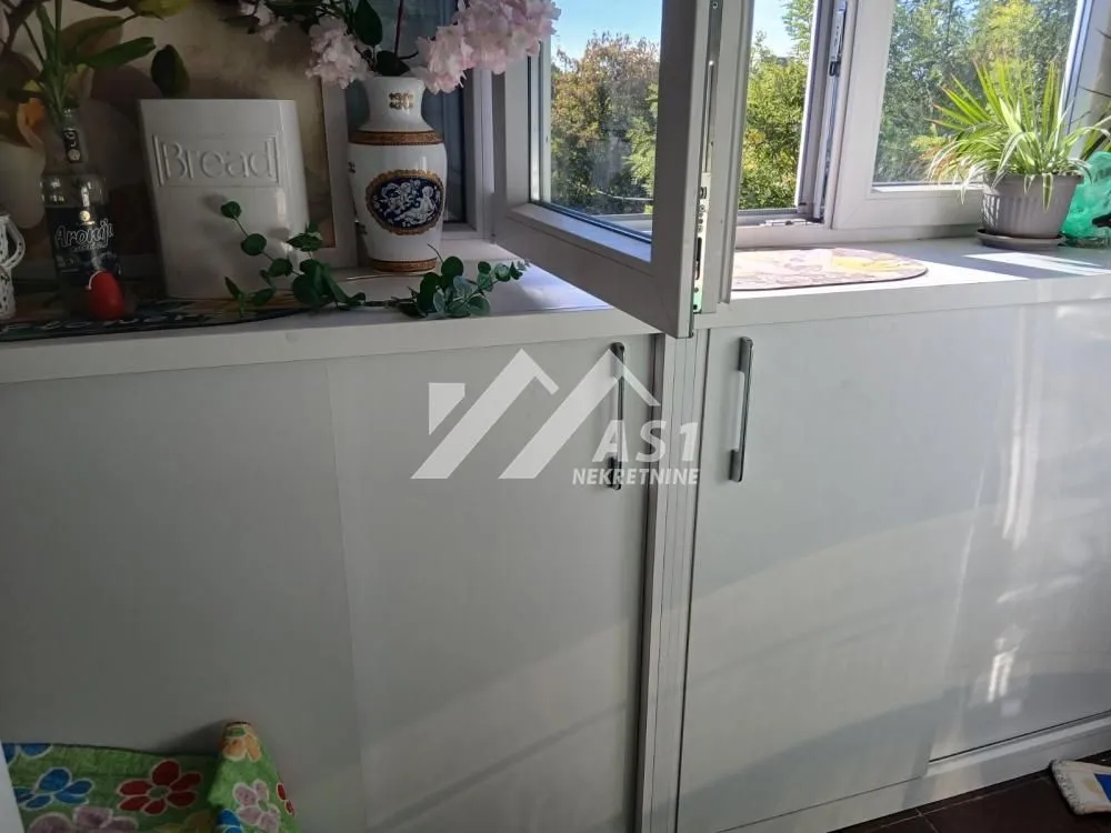 Zastakljeni balkon sa belim ormarićima i prozorom koji se otvara.