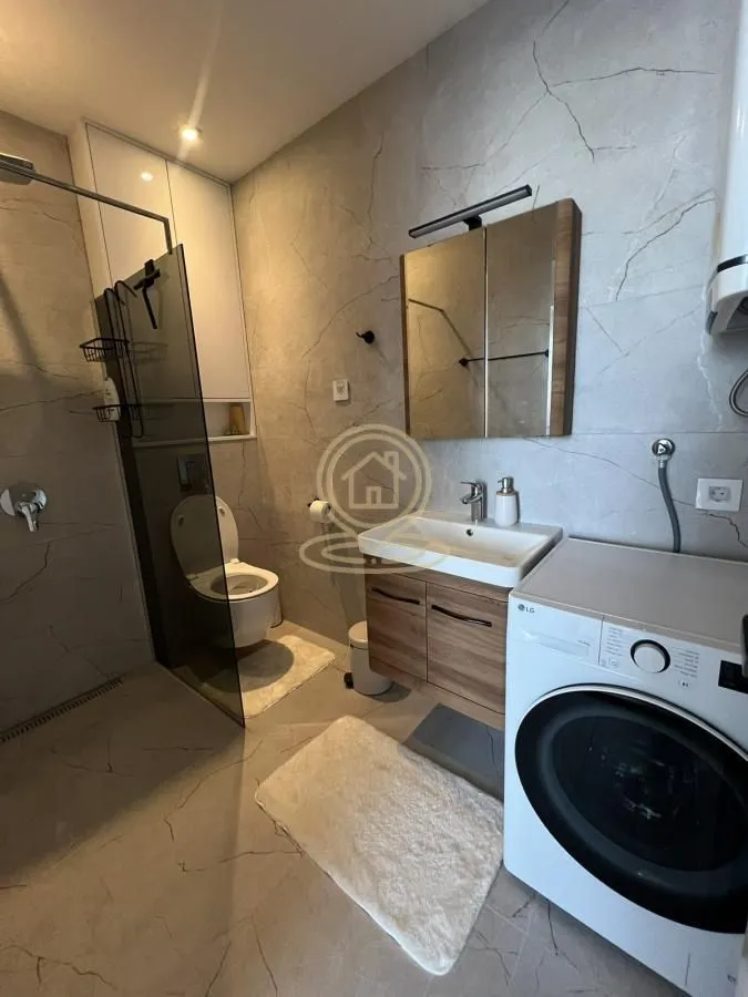 Moderno opremljeno kupatilo sa tuš kabinom i veš mašinom.