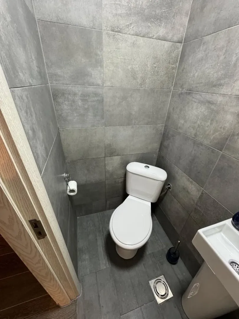 Small bathroom with grey tiles, toilet, and sink.