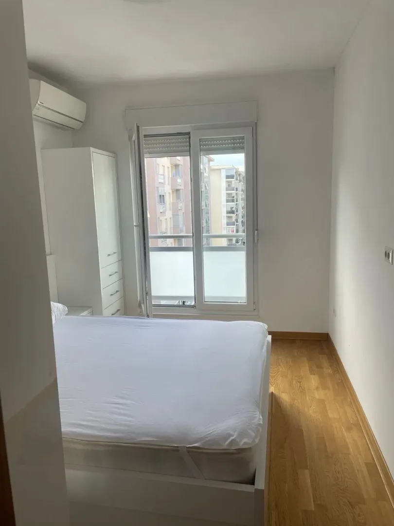 Bright bedroom with a double bed, white wardrobe, and balcony doors.