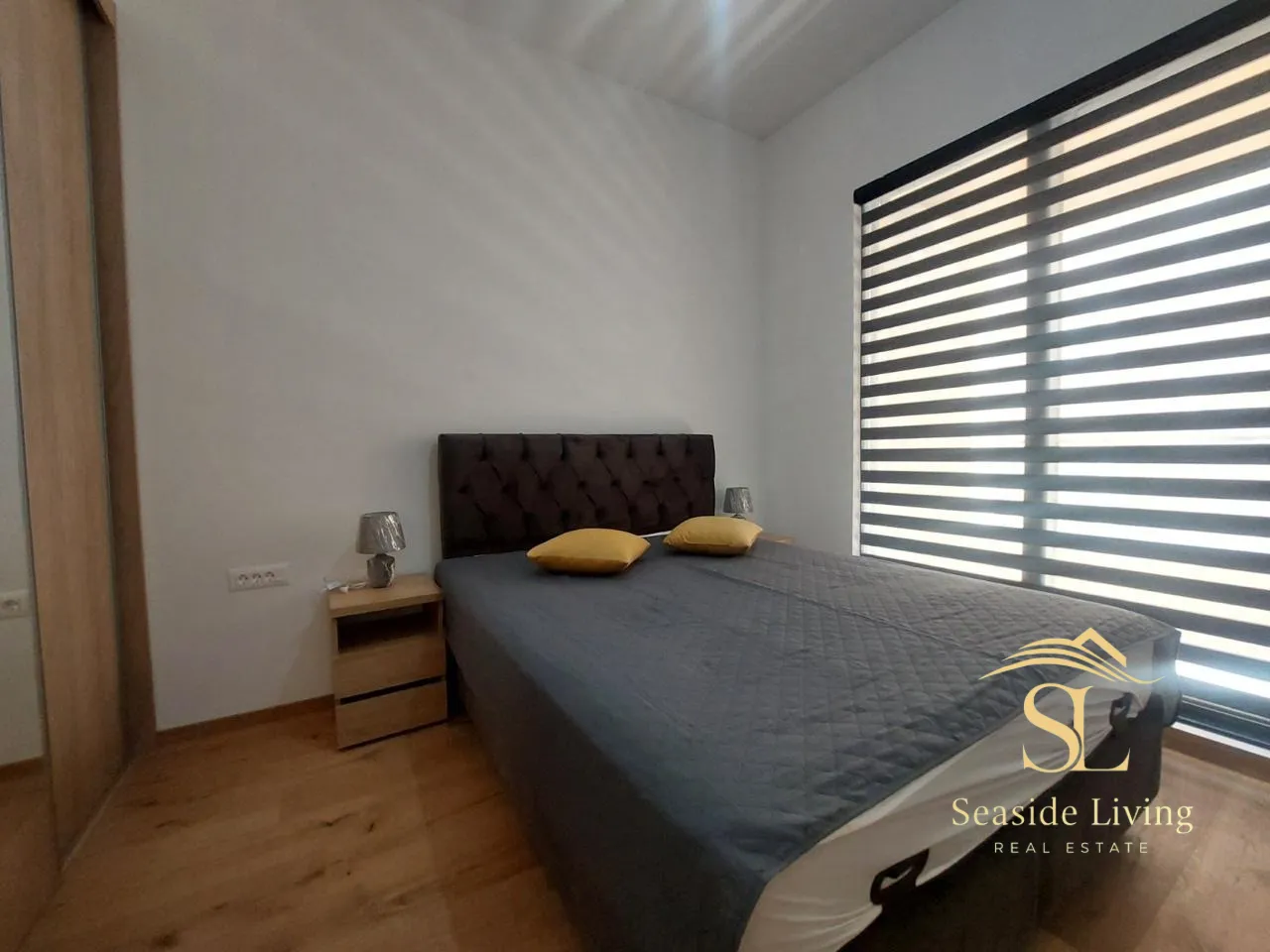 Furnished bedroom with a double bed and a window with blinds.