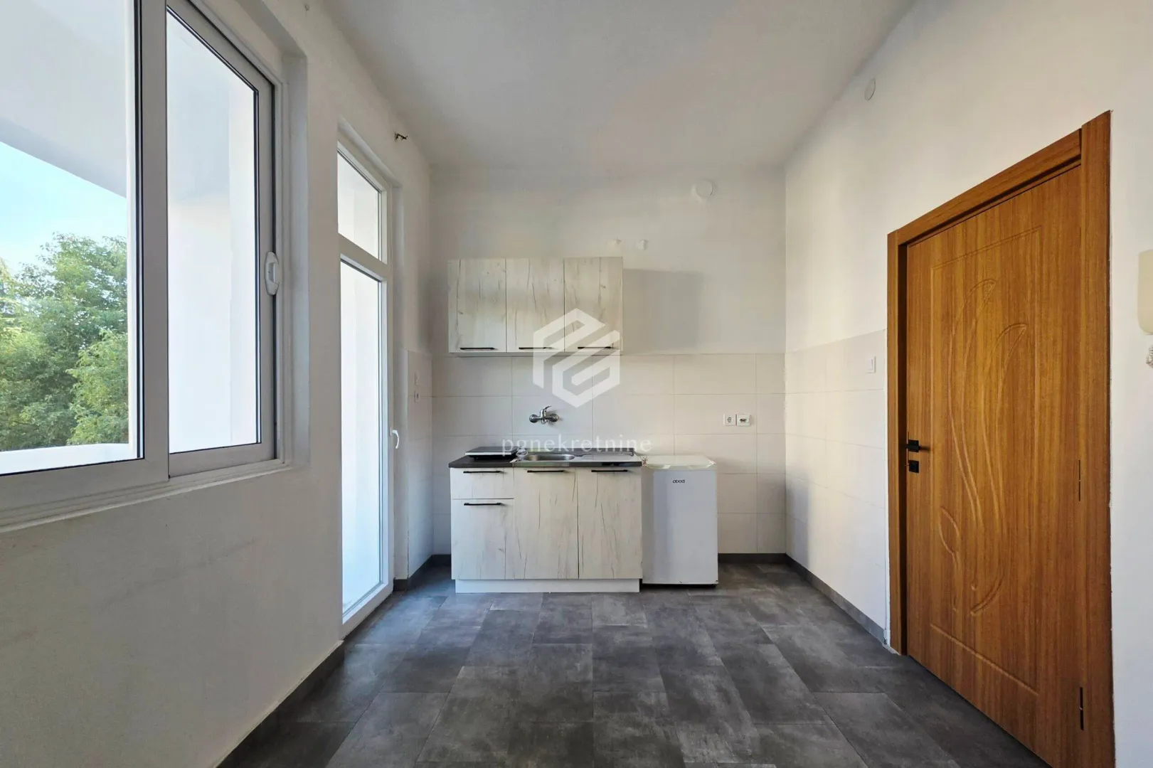 Small kitchen with white units and a refrigerator in a bright room.
