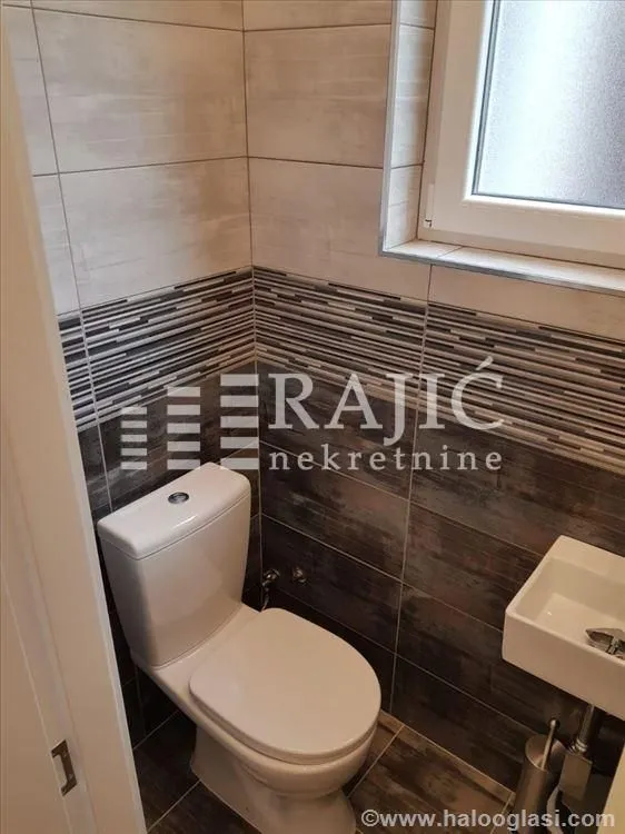 Manje kupatilo sa WC šoljom, umivaonikom i pločicama.