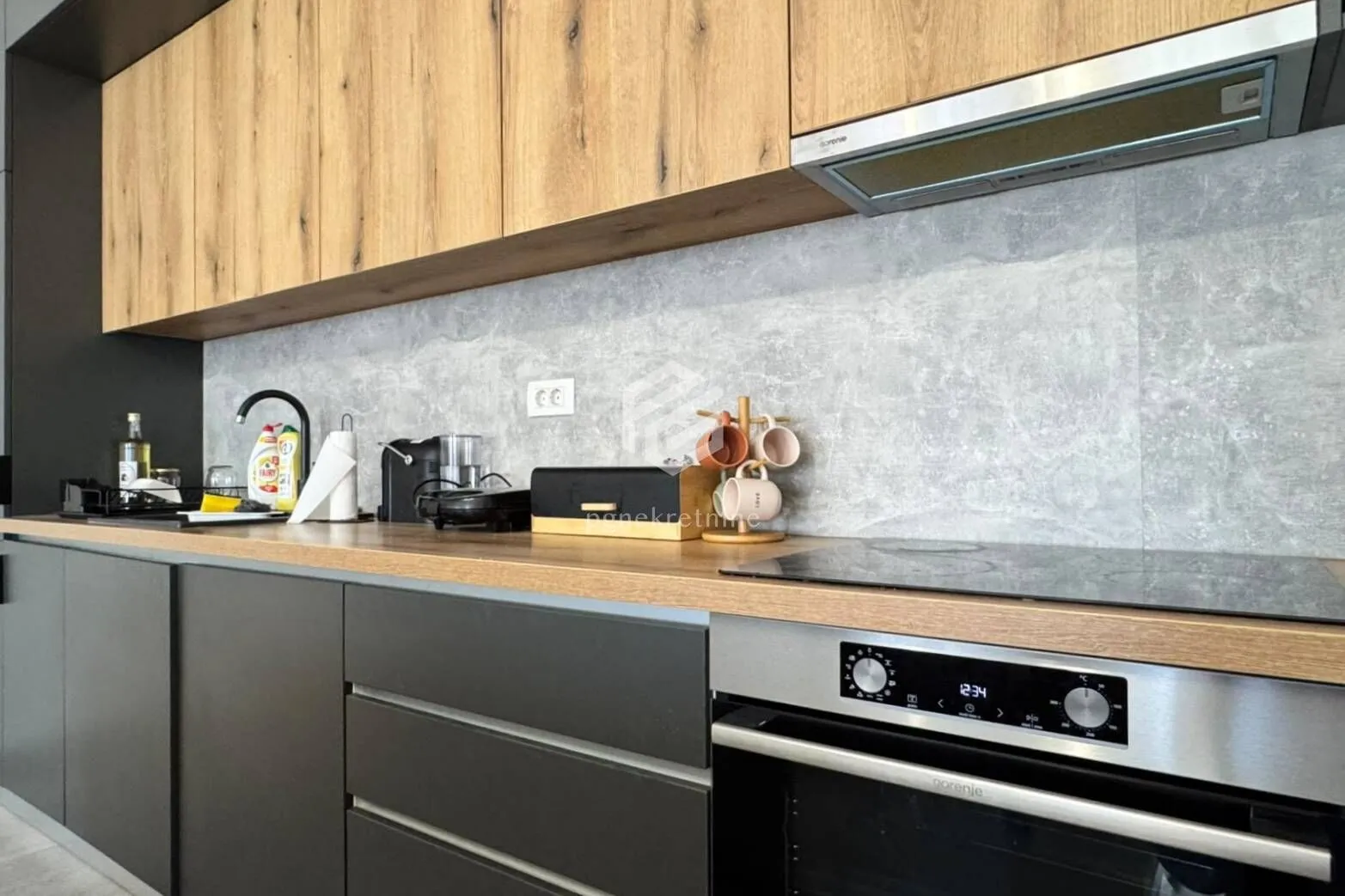 Modern kitchen with wooden upper cabinets, dark lower cabinets, and built-in oven.