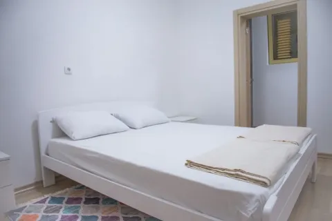 Svijetla spavaća soba sa bijelim krevetom i šarenim tepihom. - image 4