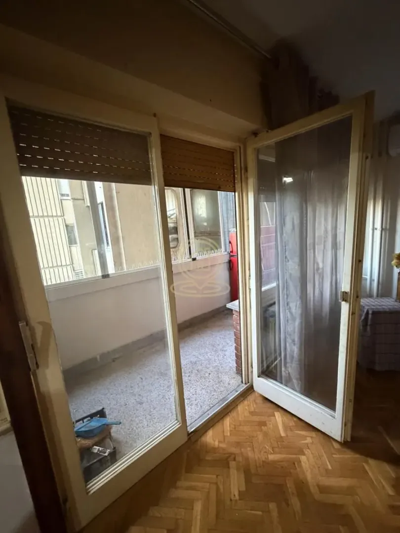 Pogled iz stana na zatvorenu terasu sa drvenom stolarijom i parketom u sobi.