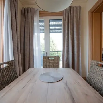 Trpezarija sa drvenim stolom i pletenim stolicama pored balkonskih vrata. - image 5