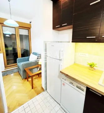 Compact kitchen with cabinetry and refrigerator, overlooking part of the living area. - image 4