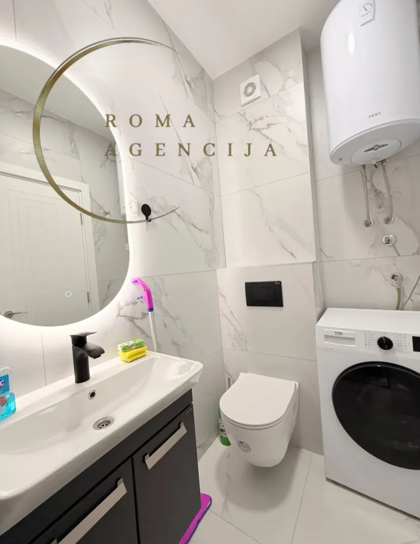 Moderne kupatilo sa umivaonikom, WC šoljom, veš mašinom i velikim ogledalom.