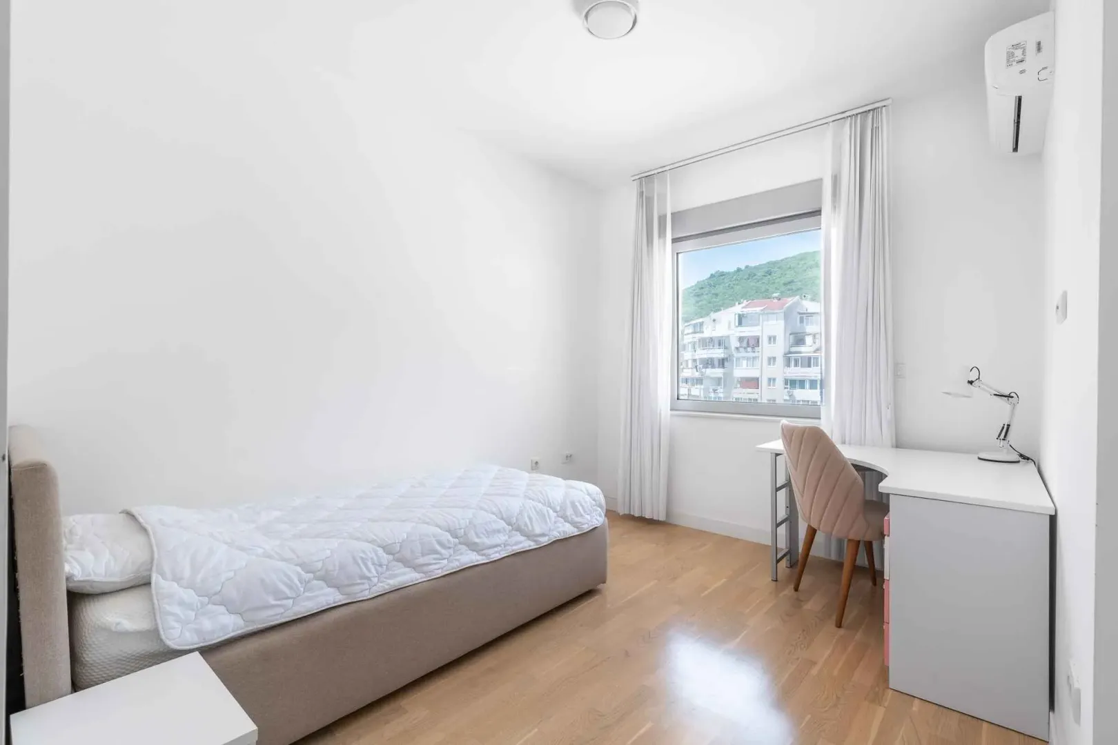 Bright bedroom with a bed, desk, and a window with a view.