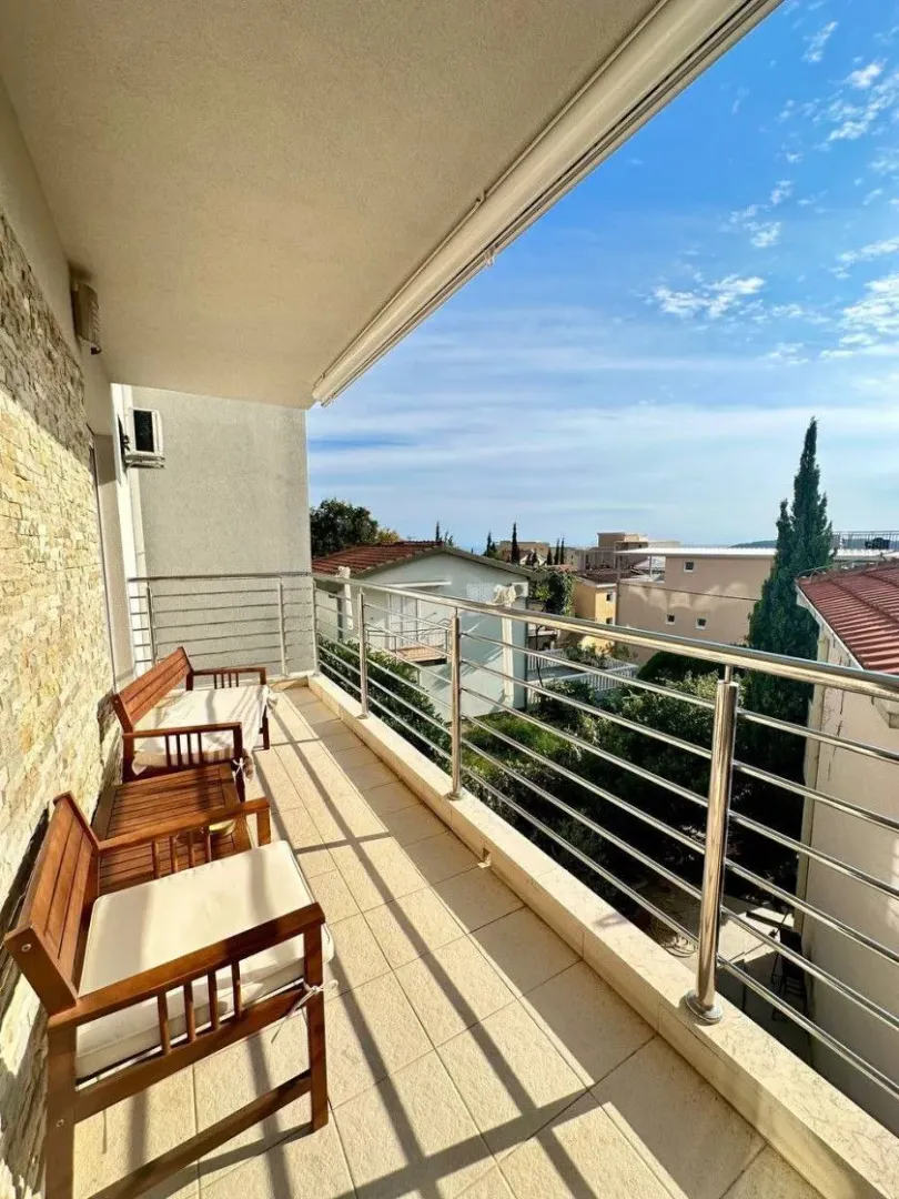 Natkriveni balkon sa drvenim namještajem i metalnom ogradom.