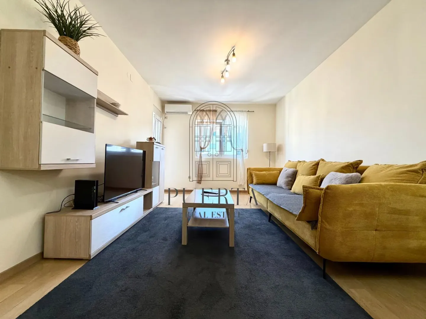 Spacious living room with a yellow sofa, TV, and light furniture.