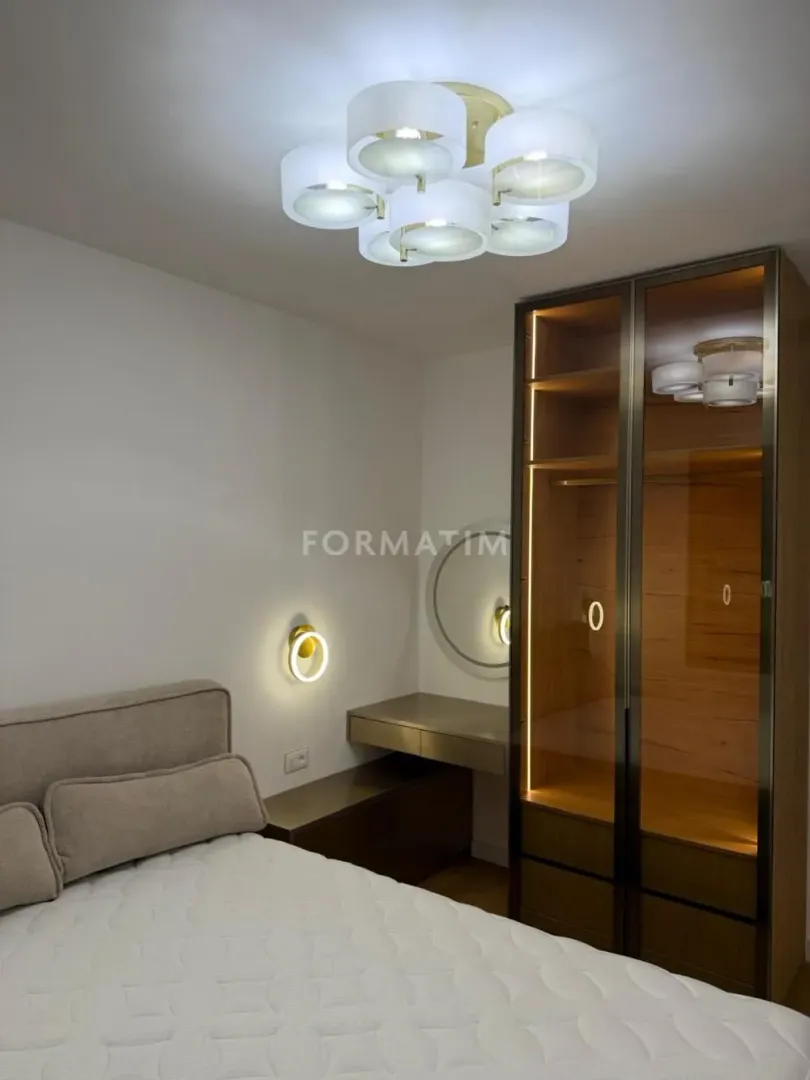 Modern bedroom with a double bed, glass-door wardrobe, and integrated lighting.
