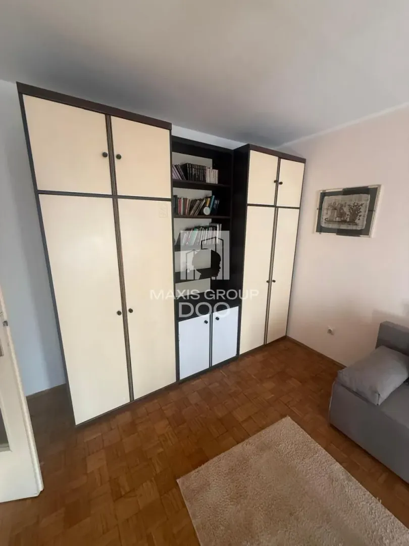 Dnevna soba sa velikim ormanom, policama za knjige i garniturom za sedenje.