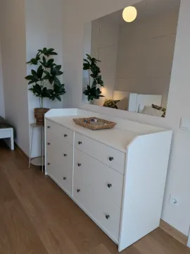 Spavaća soba sa bijelom komodom, ogledalom i dekorativnom biljkom. - image 15