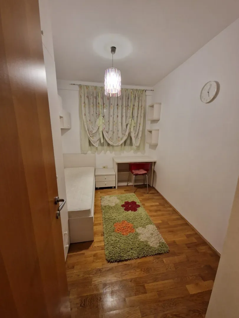 Mala spavaća soba sa jednim krevetom, radnim stolom i šarenim tepihom.