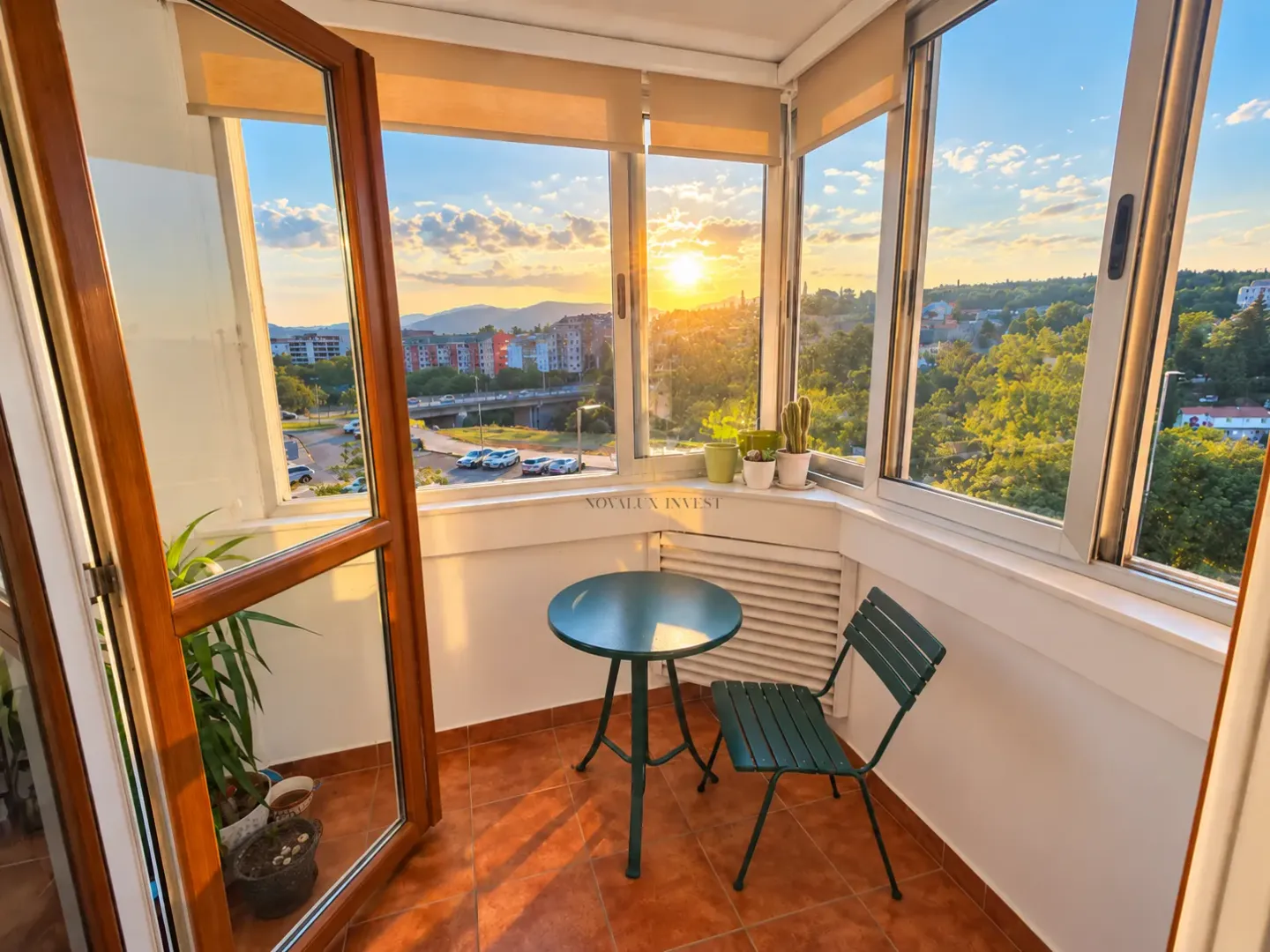 Zastakljeni balkon sa malim stolom, stolicom i pogledom na grad.