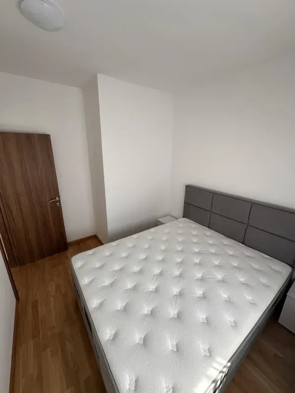 Spavaća soba sa bračnim krevetom, bijelim zidovima i drvenim podom.