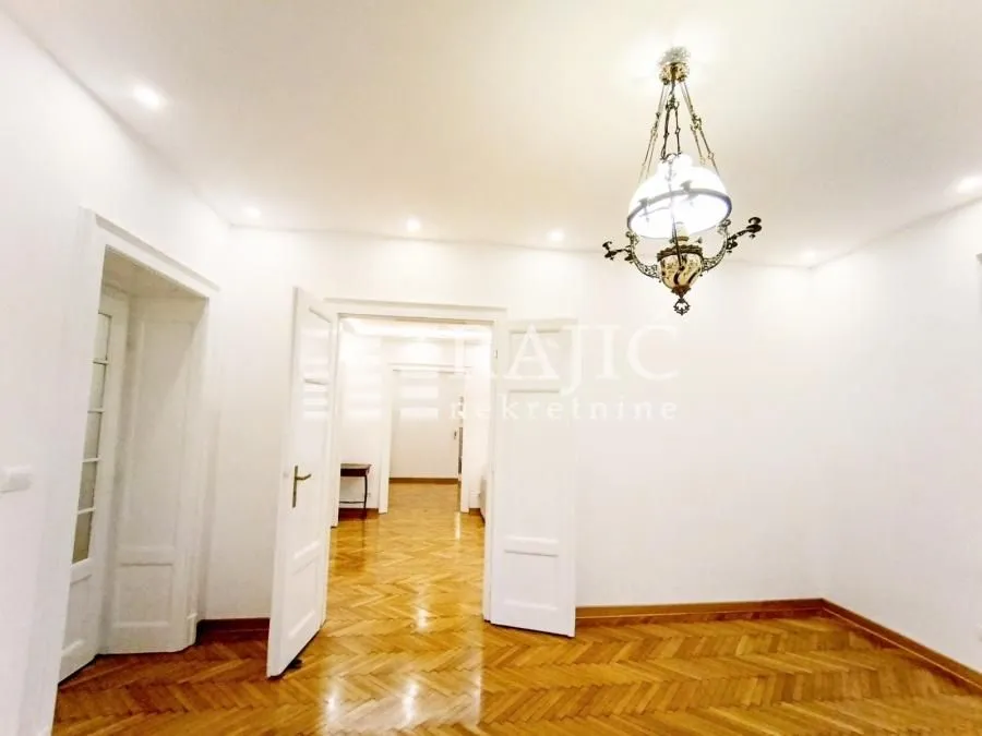Empty room with parquet flooring and a decorative chandelier.