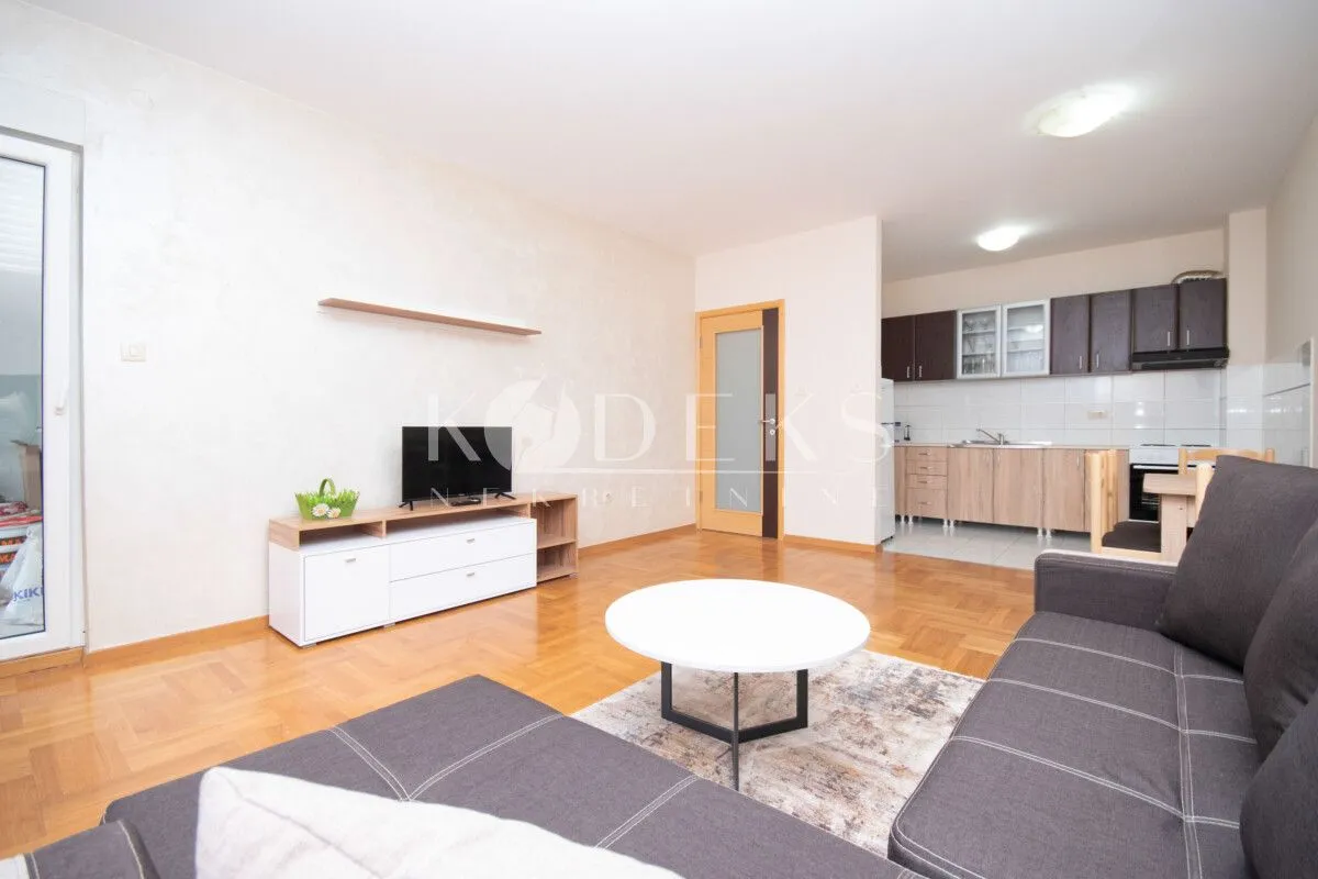 Living room with a sofa, TV unit and a view of the kitchen in the background.
