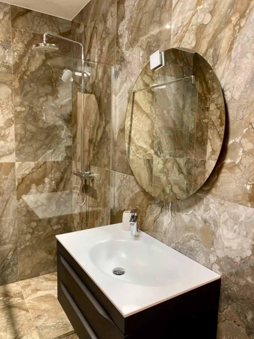 Modern bathroom with a sink, shower cabin, and round mirror.