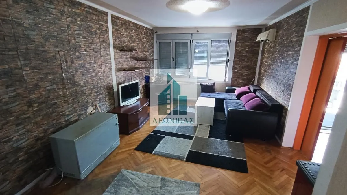 Dnevna soba sa garniturom za sedenje, televizorom i parketom na podu.
