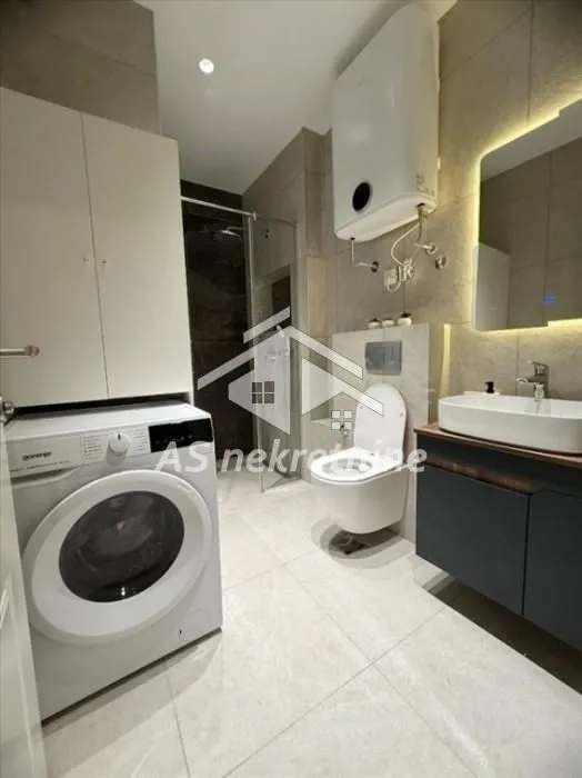 Modernly equipped bathroom with a washing machine, shower cabin, and built-in fixtures.