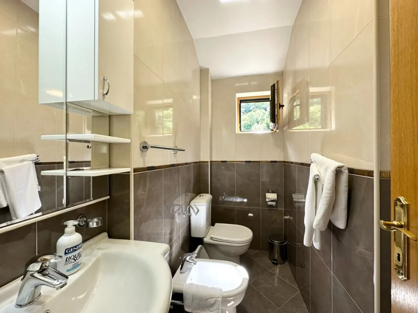 Small bathroom with a sink, toilet, bidet, and wall tiles.