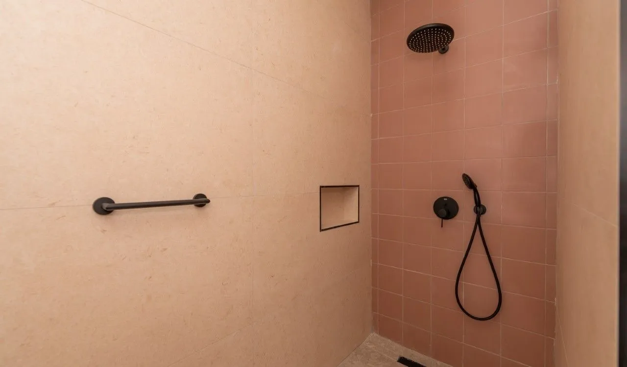 Modern walk-in shower with black fixtures and tiles in beige and pink tones.