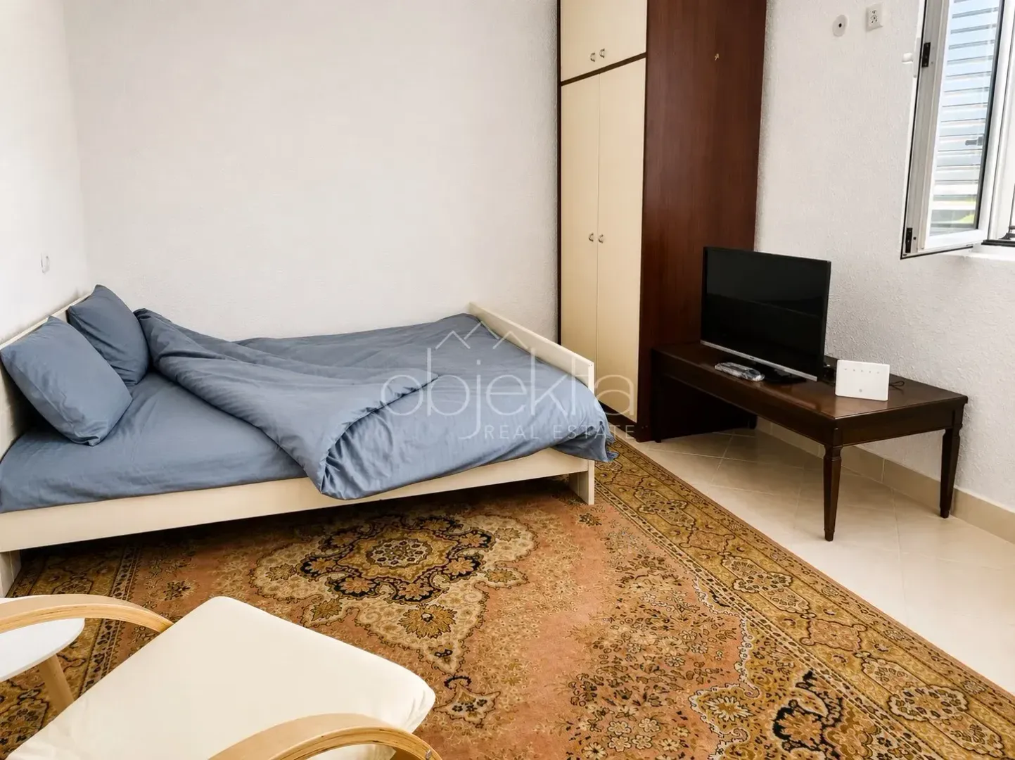 Namještena spavaća soba sa krevetom, plakarom i televizorom.