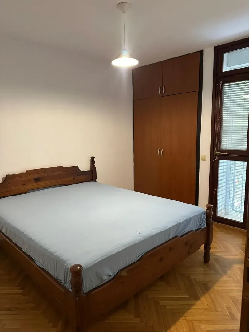 Spavaća soba sa bračnim krevetom, drvenim ormarom i parketom.
