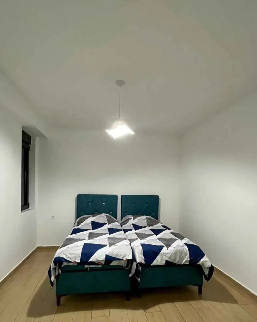 Spavaća soba sa dva spojena kreveta i bijelim zidovima.