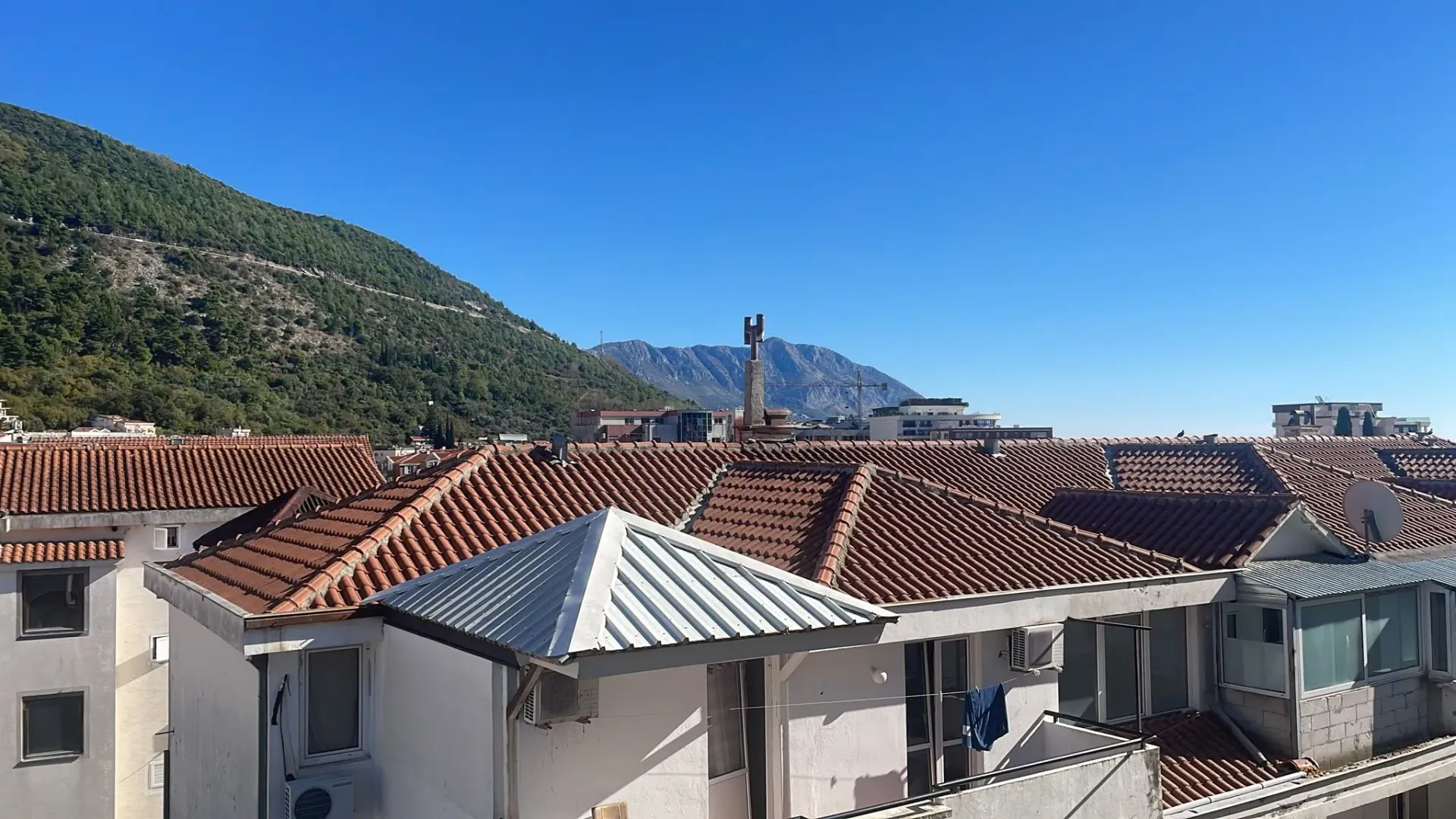 Pogled sa terase na krovove zgrada i planine u pozadini.