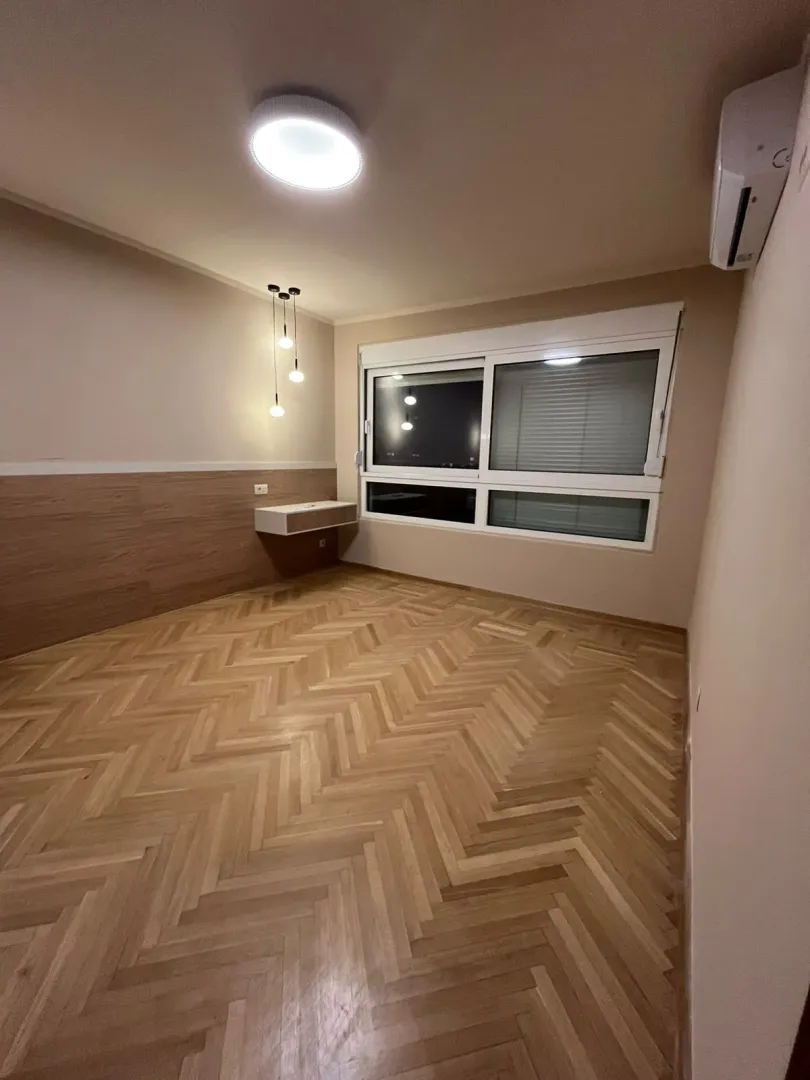 Prazna soba sa drvenim podom, prozorom i klima uređajem.