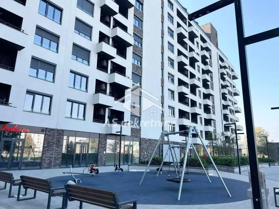 Pogled na modernu stambenu zgradu sa dečijim igralištem u dvorištu.