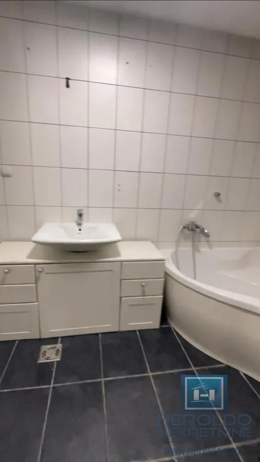 Kupatilo opremljeno umivaonikom sa ormarićem i ugaonom kadom.