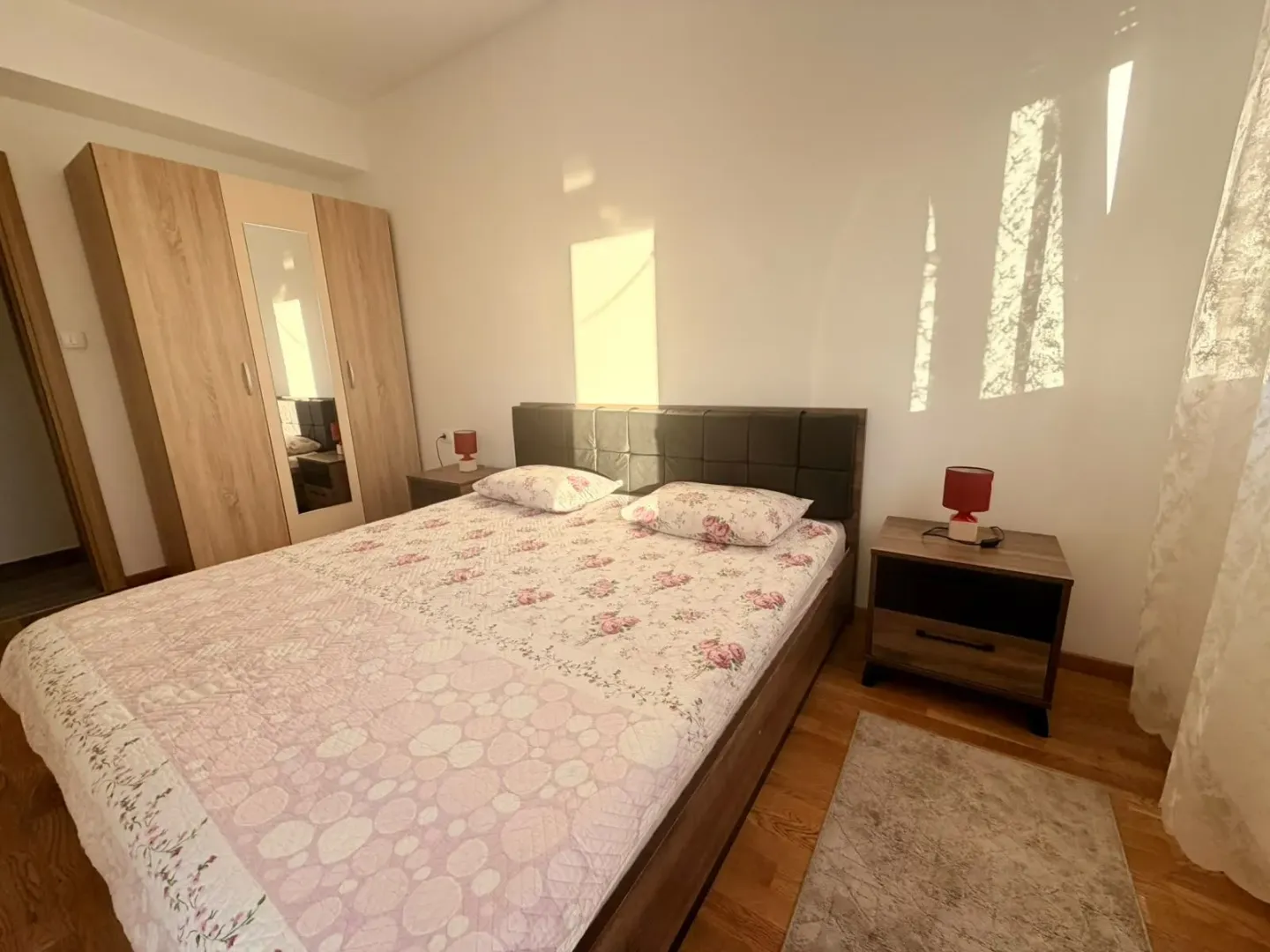 Svjetla spavaća soba sa bračnim krevetom, ormarom i noćnim stočićima.
